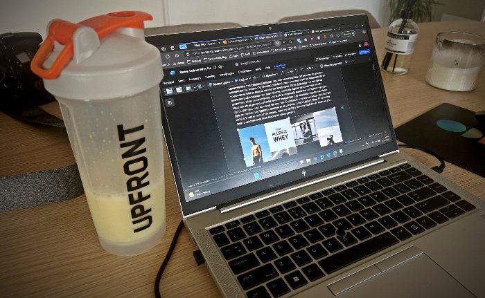 Je ziet het concept van dit blog artikel op een laptop open staan, links van de laptop staat een Upfront shakebeker met oranje dop