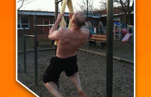 Man met ontbloot bovenlichaam voert een pull up aan een handdoek uit