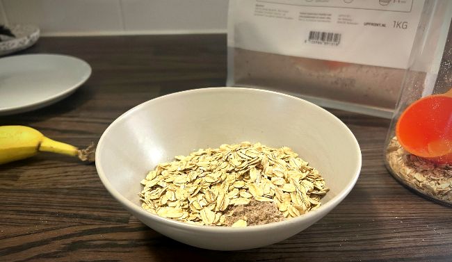 Een kom met Upfront eiwit oats en daarbovenop een extra schep havermout