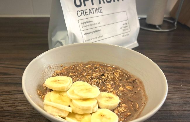 Een kom bereide Upfront Eiwit Oats chocoladesmaak met schijfjes banaan erbovenop