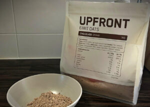Zak Upfront eiwit oats chocoladesmaak en daarvoor een schaaltje waar de oats in zitten